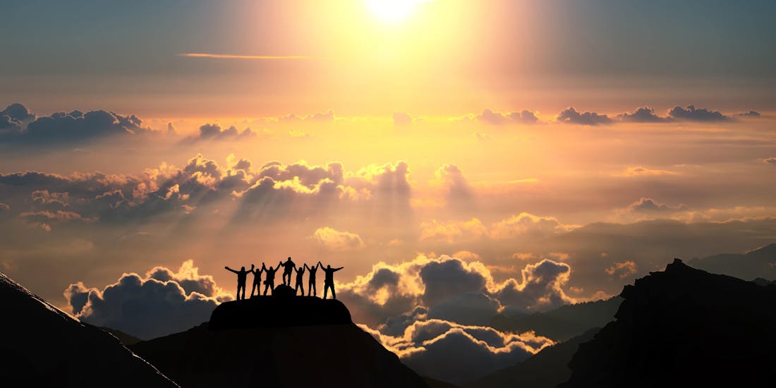 The motivated team of Olimpionico Sport 2 is stood on top of a mountain looking at the sunset after a successful day full of new experiences for their customers.