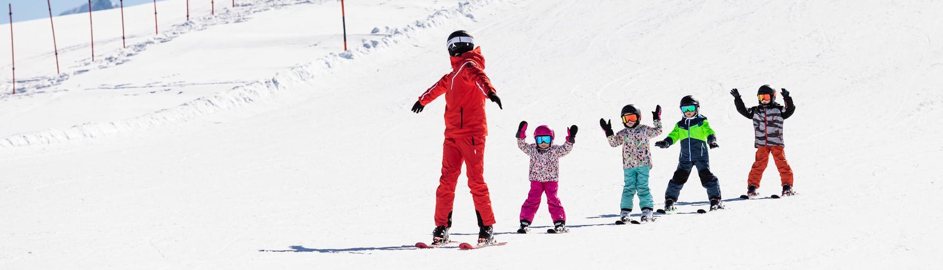 Maestro di sci e bambini che sciano sulle piste durante una lezione di sci.
