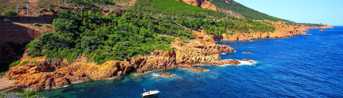 Boat Trips Saint-Raphaël SEM Hero Schilderachtig uitzicht op de kust met rode rotsen en turquoise zee in Saint-Raphaël, Provence, onder een heldere blauwe lucht.