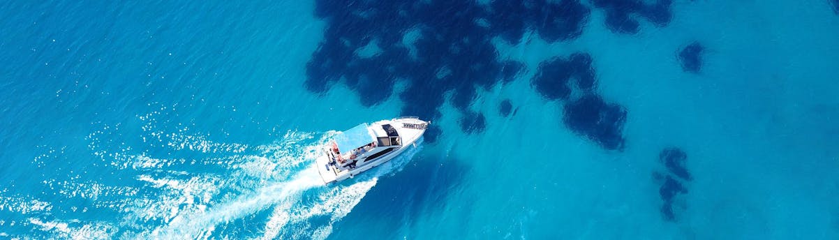 Boat Trips Petite Terre SEM Hero Ein Boot gleitet sanft über das lebendige blaue Wasser unter einem klaren Himmel.
