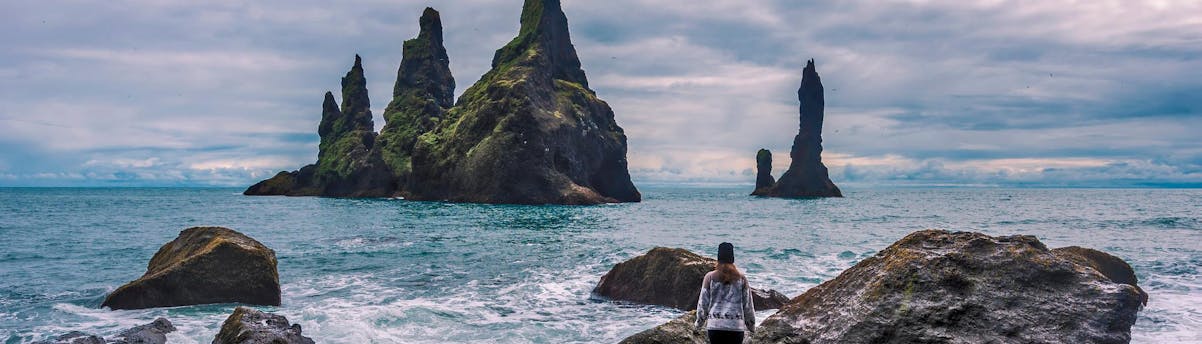 Sightseeing & Bus Tours Reynisfjara Beach SEM Hero Una chica se acerca a la orilla del mar frente a los acantilados de basalto, en el sur de Islandia, en la playa de Reynisfjara.