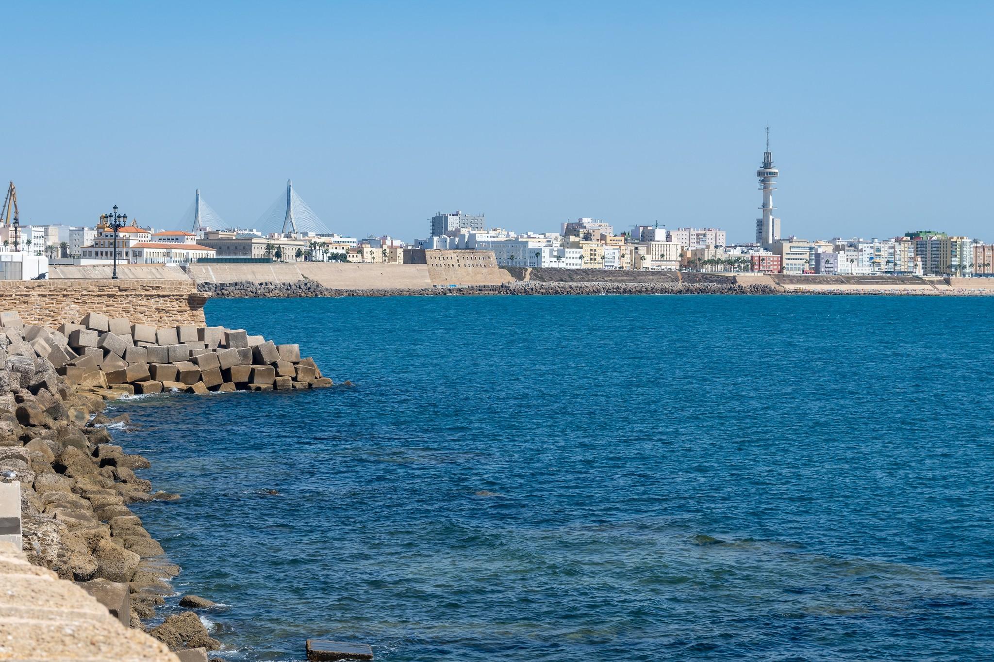 Küstenblick auf Cádiz mit Booten im Meer und Gebäuden im Hintergrund.
