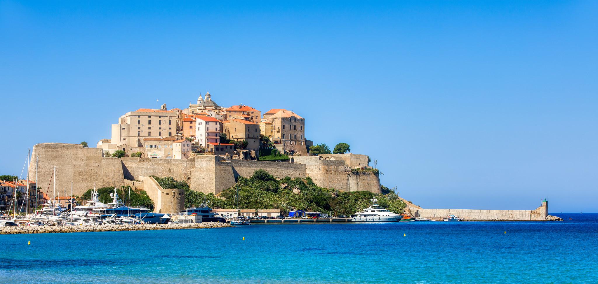 Vista aérea de Calvi, en Córcega, con la ciudadela histórica, el mar turquesa y barcos amarrados.