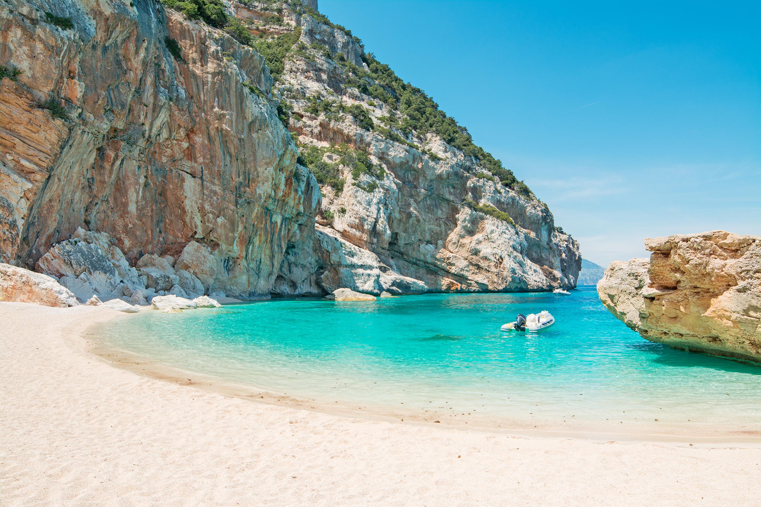 Un bateau flotte sur une eau turquoise cristalline près des falaises de Cala Mariolu.