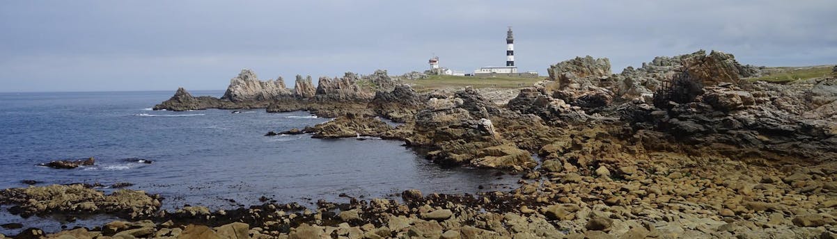 Boat Trips Ushant SEM Hero Panoramisch uitzicht op het eiland Ouessant met de historische vuurtoren, de rotsachtige kustlijn en de kalme zee.