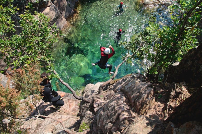 Un amateur de canyoning saute dans une piscine naturelle vert émeraude sous la supervision d'un guide de canyoning qualifié d'Acqua et Natura qui propose des sorties canyoning en Corse.