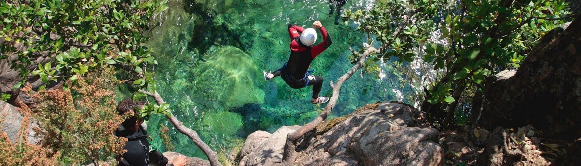 A canyoning enthusiast is jumping into an emerald green natural pool under the supervision of a qualified canyoning guide from Acqua et Natura which offers canyoning trips in Corsica.