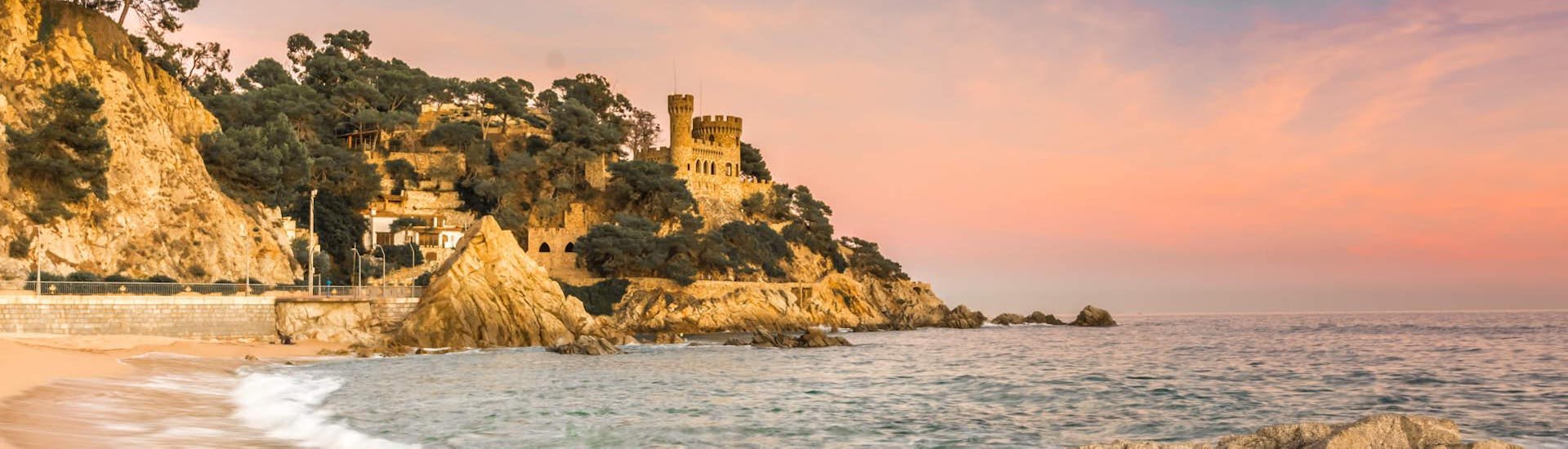 A stunning seaside town with a medieval castle, rocky shores in Lloret de Mar at sunset with Dolphins Diving Center.
