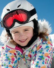 Wide shot kid with helmet smiling with mountains and blue sky in background
