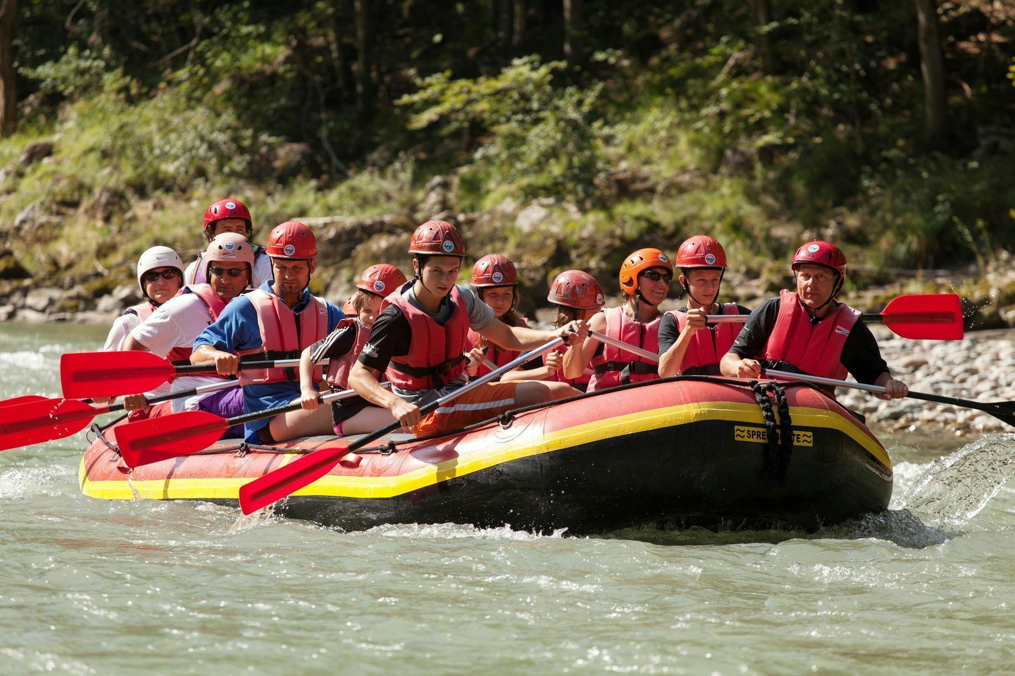 Adventure Club Kaiserwinkl Kössen Eine Gruppe von Menschen, die gemeinsam eine Rafting-Aktivität auf einem Boot genießen und zusammen paddeln.