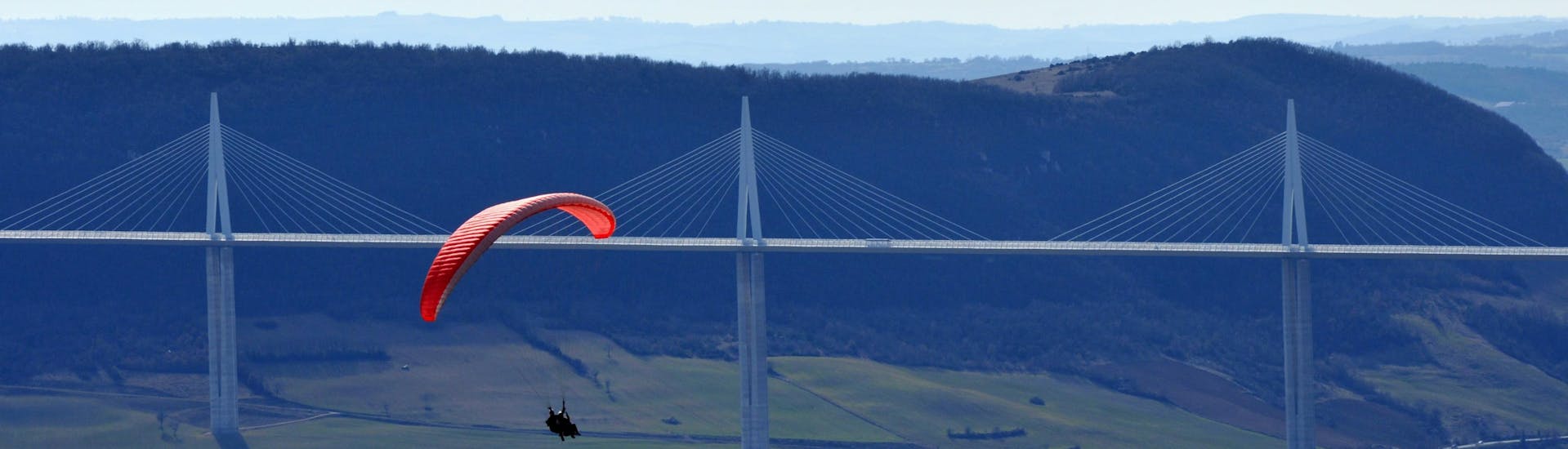 A paragliding pilot from Air Magic Parapente is doing a Tandem Paragliding Flight in front of the Millau Viaduct.