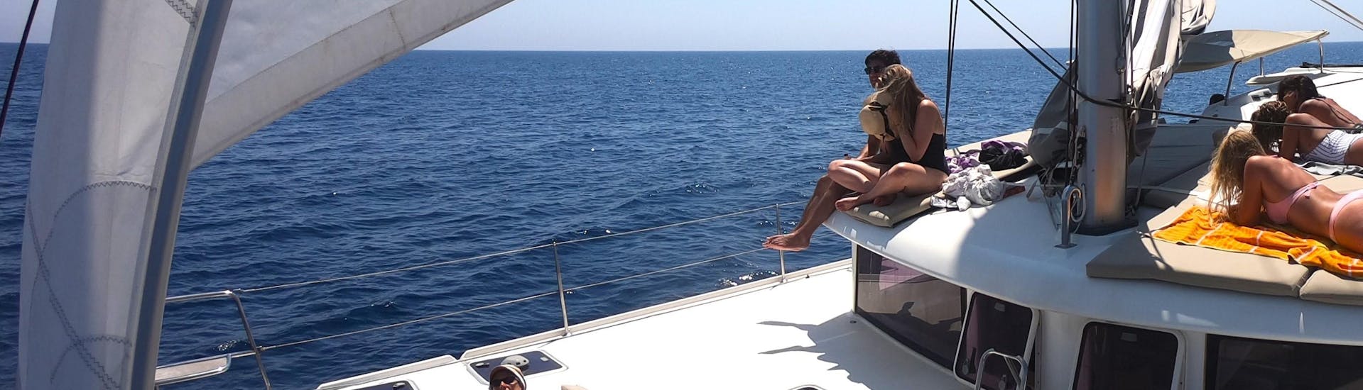 Some participants are enjoying the sun during a catamaran trip with All Sailing Alghero.