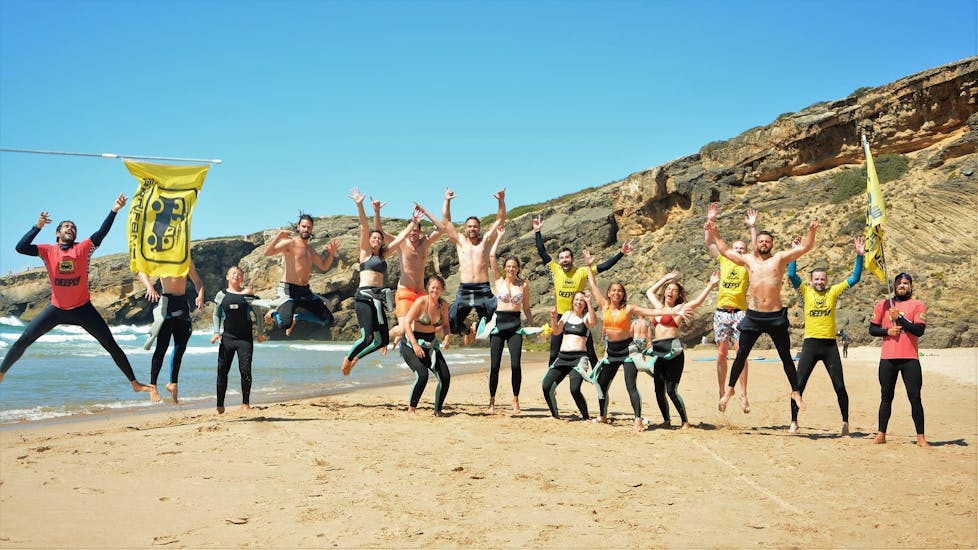 A group of happy surfers is jumping together with their surf instructors from Arrifana Surf School at the Praia da Arrifana in Arrifana.