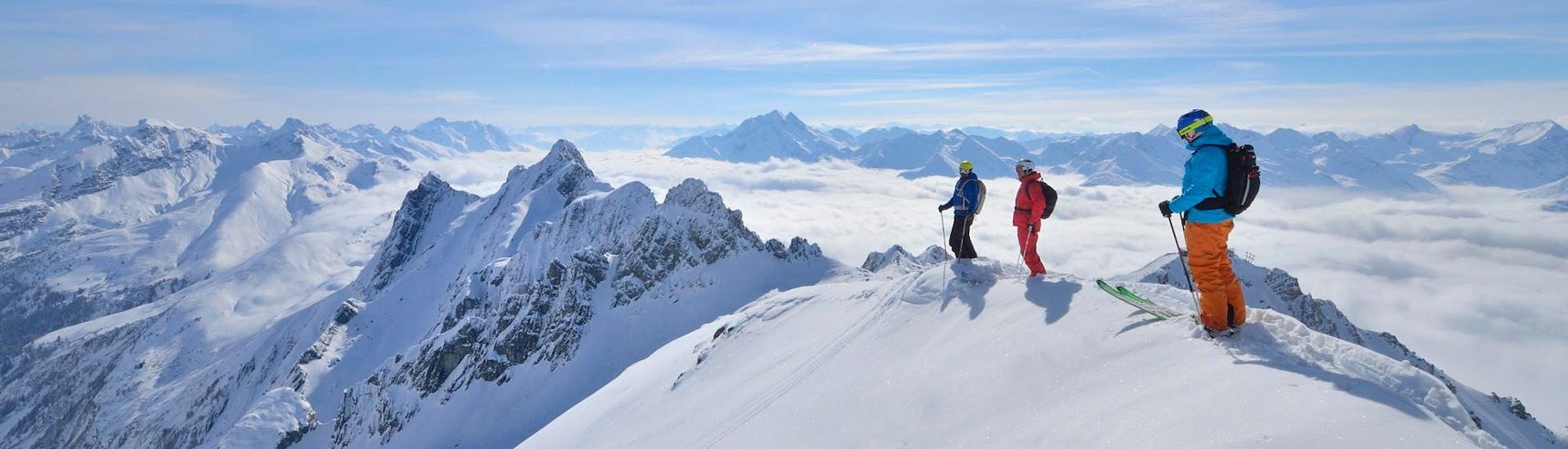 Three skiers stood on the top of a mountain, overlooking a snow-covered Alpine panorama as they prepare for an Avalanche Training, LVS Introduction session with Freeride Hotspot.