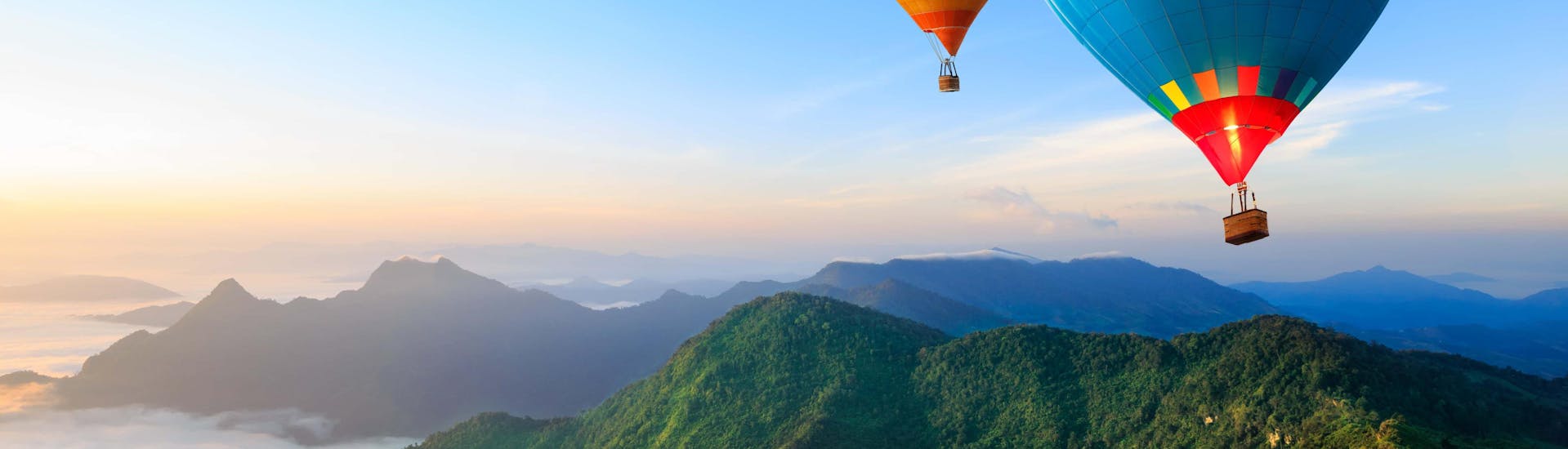 2 hot air balloons flying over a mountain landscape near the sea.