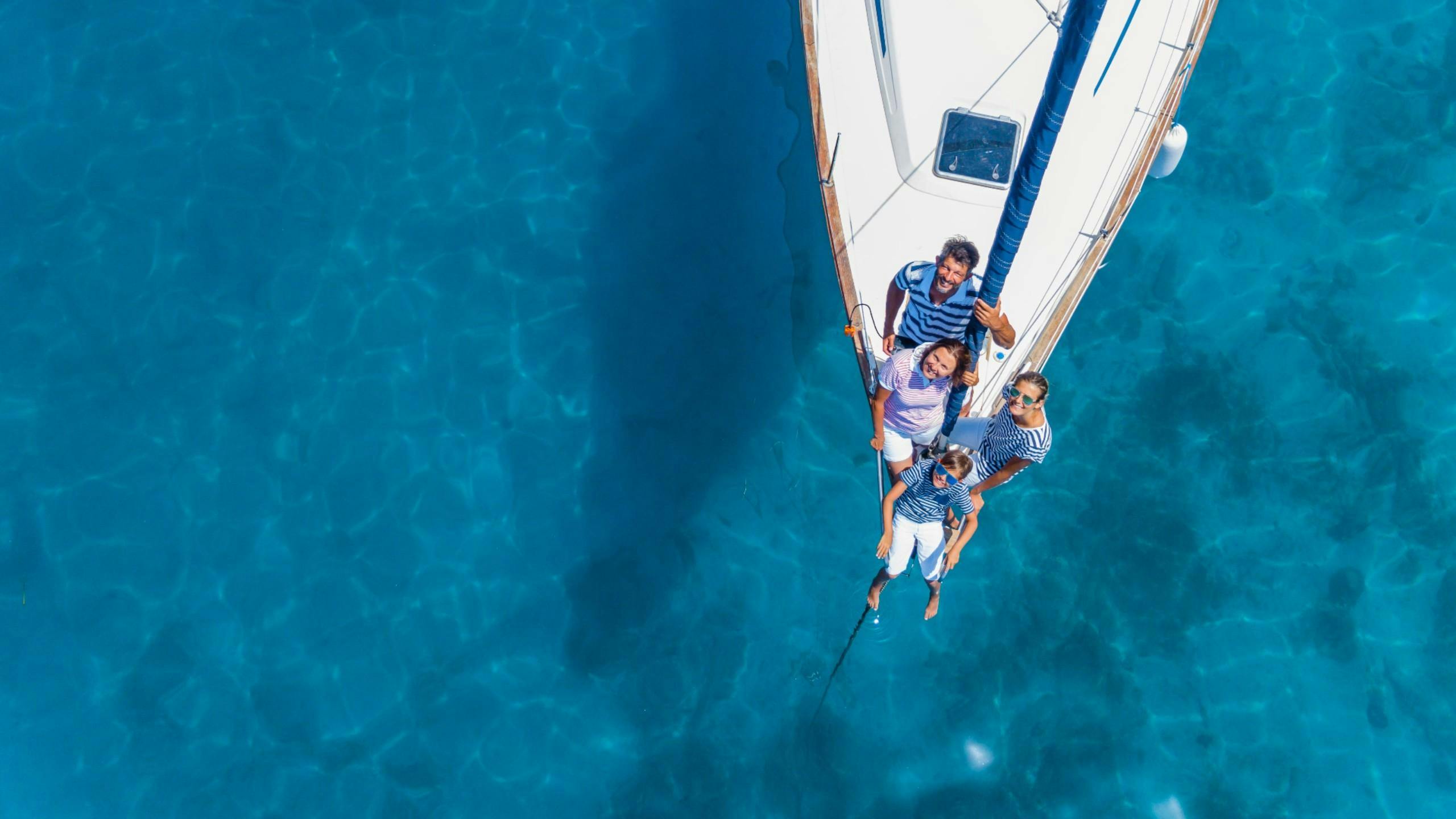 Eine Familie segelt mit einem vom Bootsverleih geliehenen Segelboot über glasklare Gewässer.