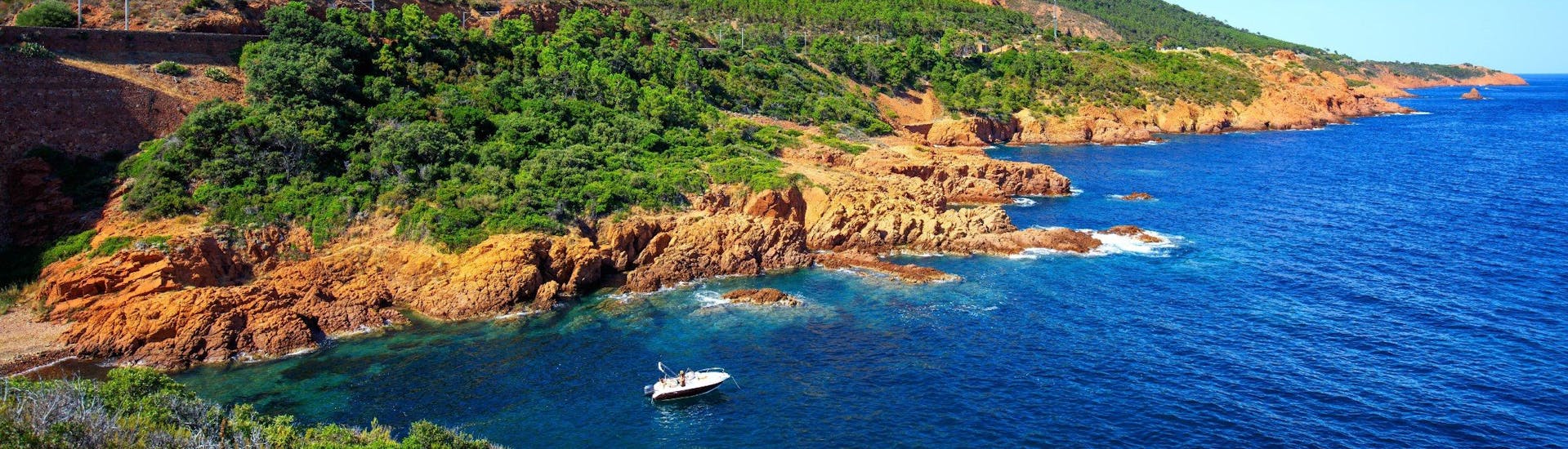 A boat is cruising along the coastline of the L'Estérel Natural Park, which is a popular destination for boat trips from Cannes.