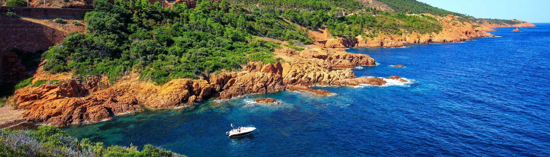 Ein Boot fährt entlang der Küsten des Naturparks L'Estérel, der ein beliebtes Ziel für Bootstouren von Cannes aus ist.