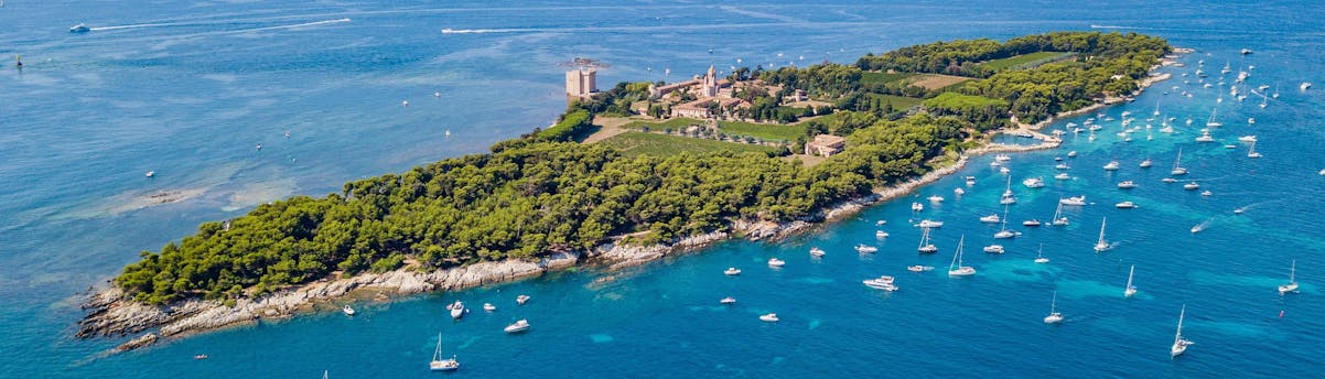 boat-trip-lerins-islands_SEM-Resort-Hero Zahlreiche Boote ankern in der Nähe der Île Sainte-Marguerite, die ein beliebter Zwischenstopp bei Bootstouren zu den Îles de Lérins ist.