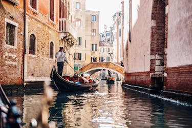 A gondolier is paddling through a narrow canal on a gondola ride in Venice.