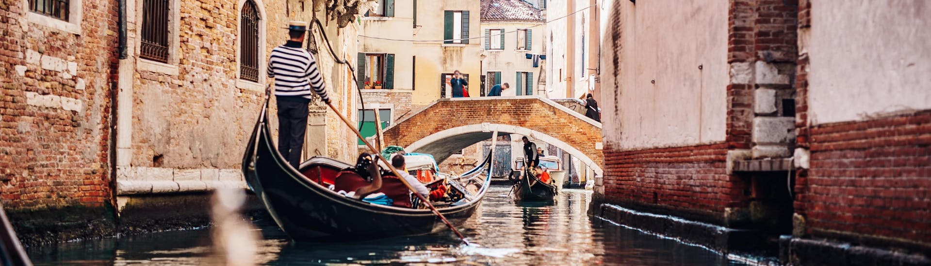 A gondoliere is paddling the boat through a narrow canal on a gondola ride near the Grand Canal in Venice.