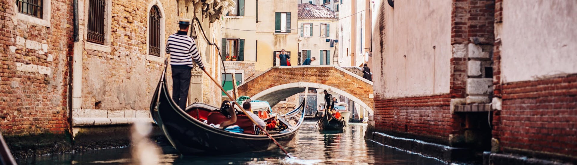 A gondolier is paddling through a narrow canal on a gondola ride in Venice.