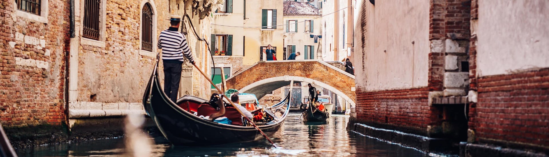 A gondoliere is paddling the boat through a narrow canal on a gondola ride in Venice.