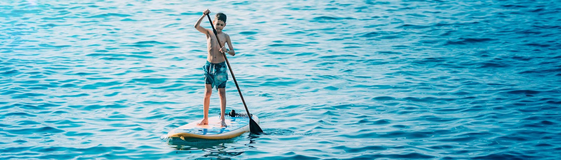 A kid on a board during a boat trip with SUP boards included on board.