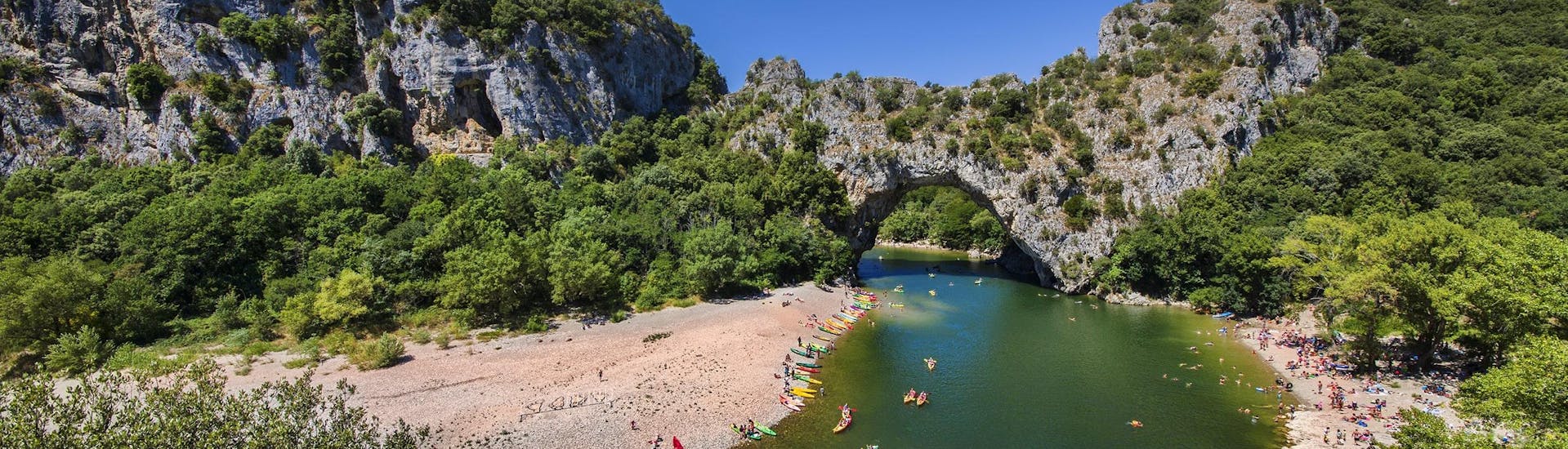 A group of people is paddling through the Pont-d'Arc while canoeing in Ardèche.