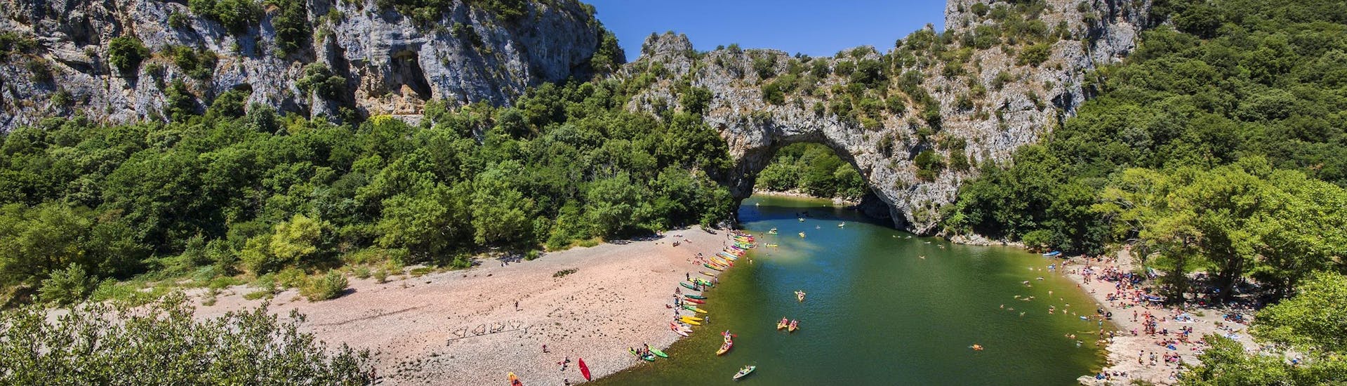 A group of people is paddling through the Pont-d'Arc while canoeing in Ardèche.