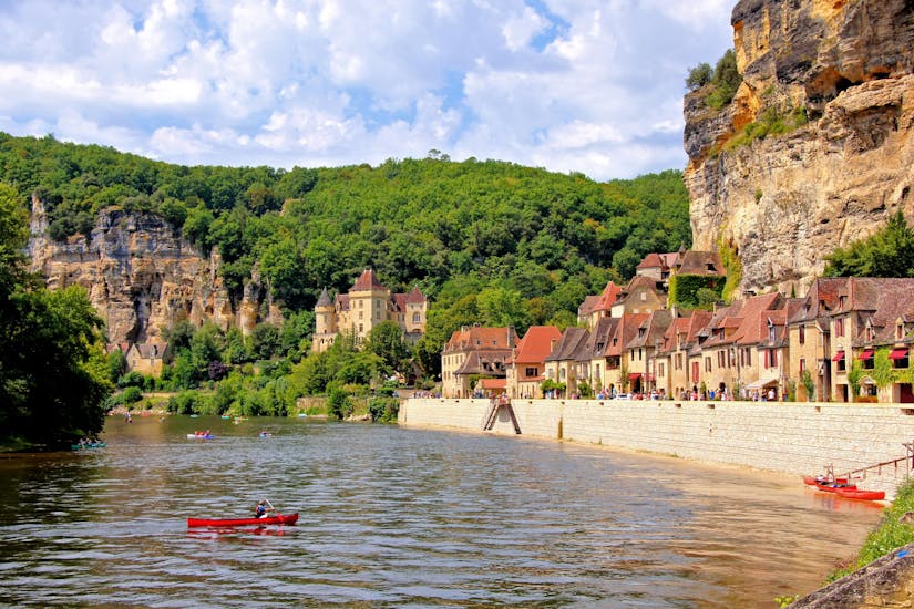 Some people are paddling in canoes on the Dordogne River in front of a village with a castle with Canoe Randonnée Dordogne.
