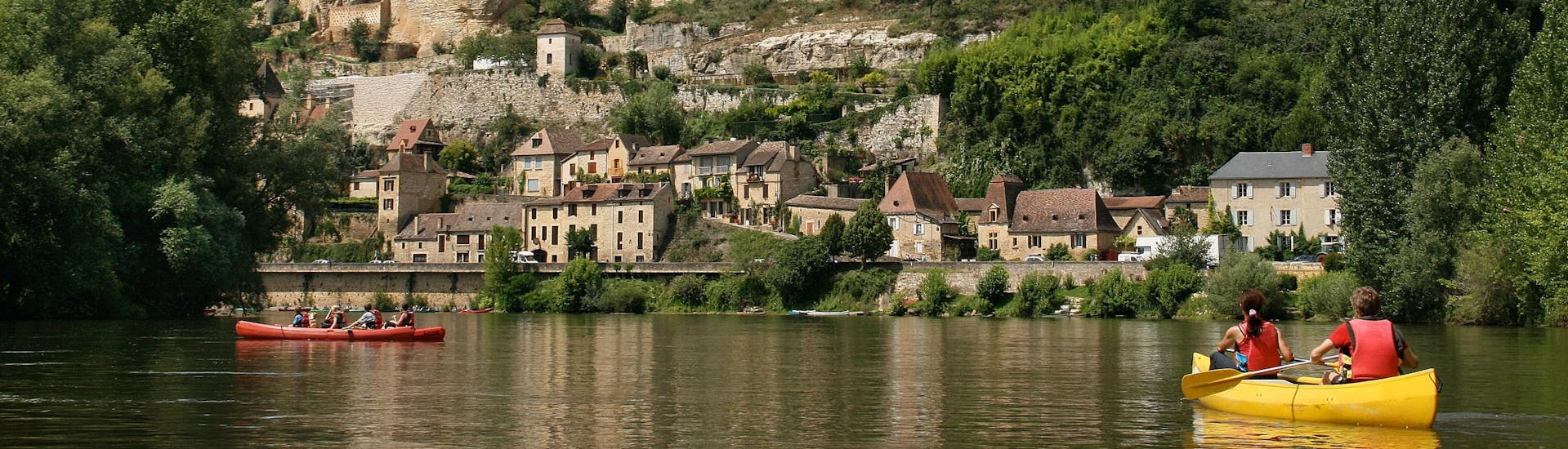 Holidaymakers are taking advantage of their holidays to take a canoe trip on the Dordogne River, and are paddling underneath the Beynac Castle.