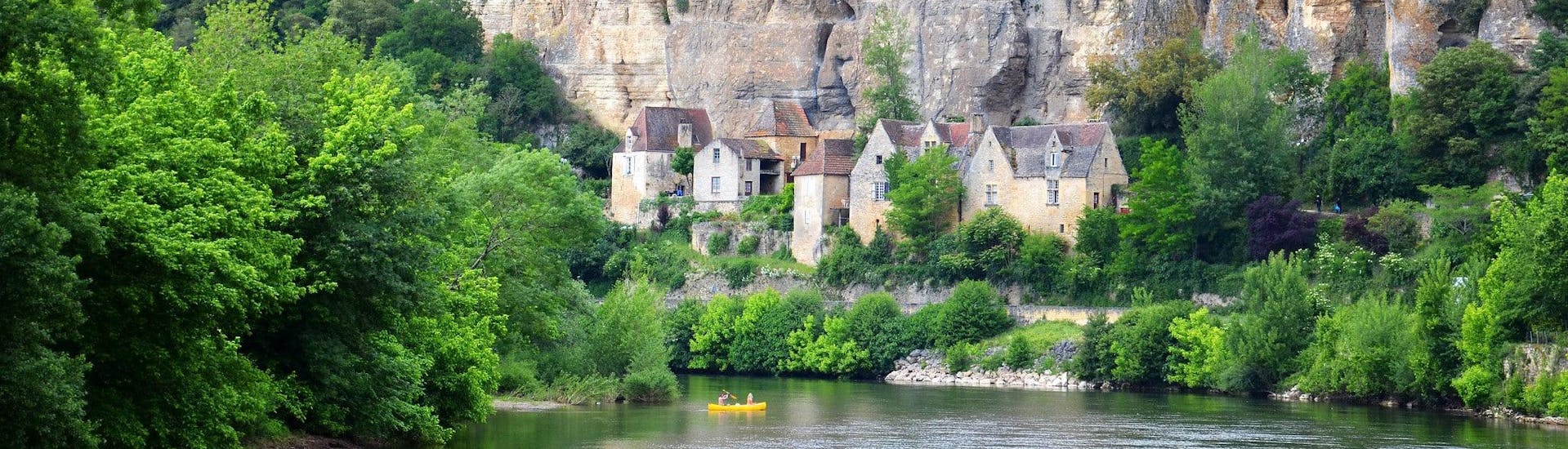 Canoe enthusiasts are paddling quietly on the Vézère river in the Dordogne in front of the troglodytic habitats of the town of Les Eyzies.