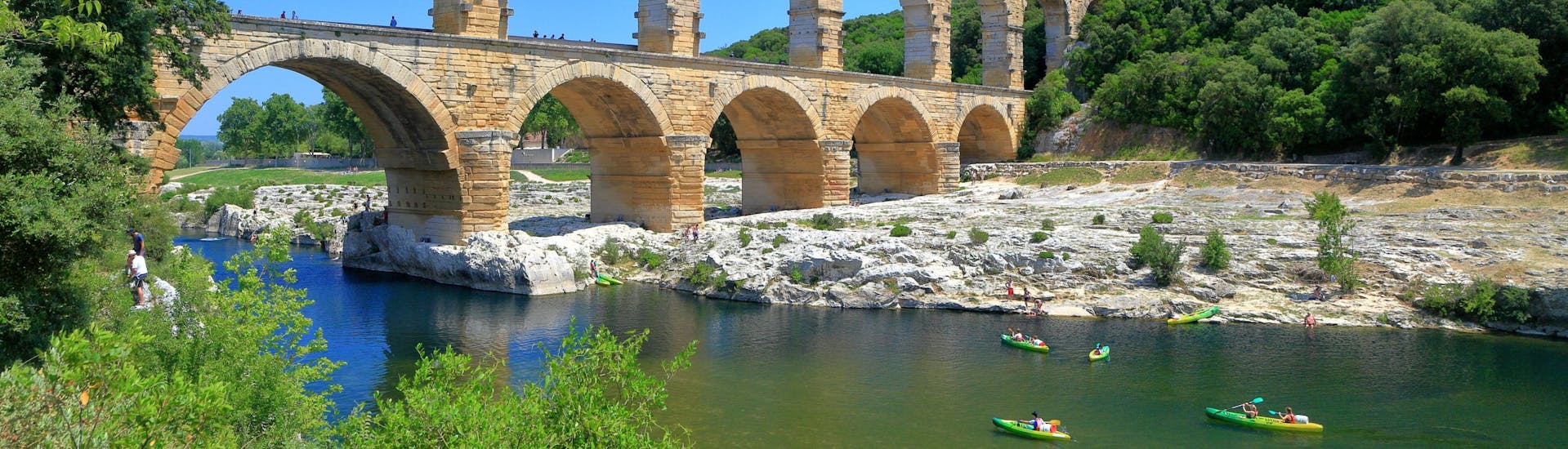 Holidaymakers are paddling on the river Gardon under the Pont du Gard bridge with their canoe.