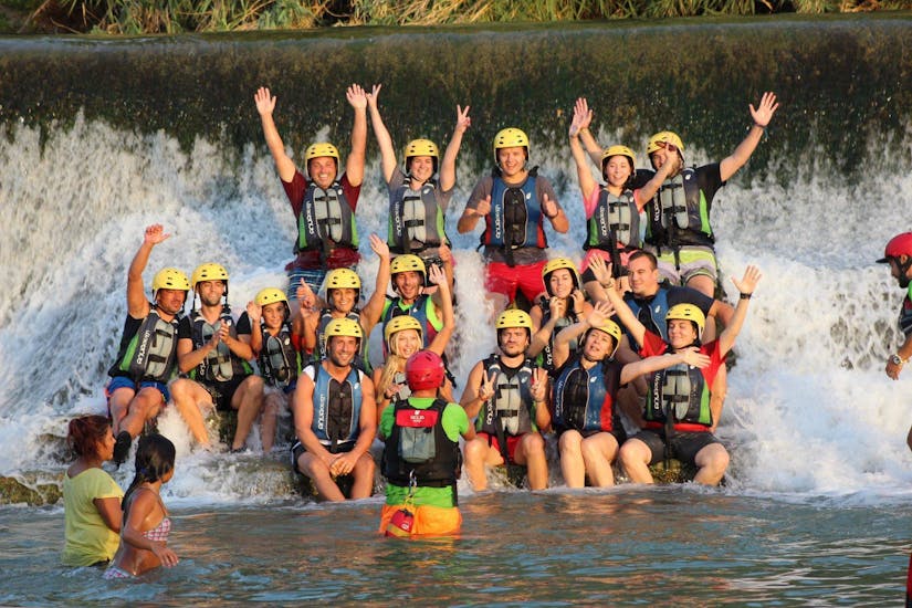 A group of participants smiles into the camera as they stand under a waterfall together with Cañón y Cañón Multiaventura Murcia.