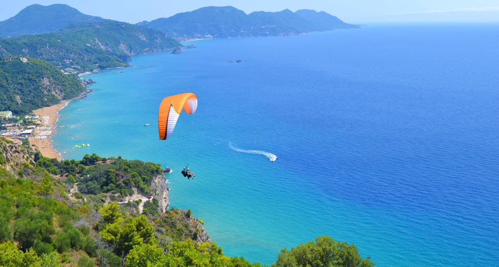 Atandem pilot from Corfu Paragliding and his passenger are gliding over the turquoise water of the Ionian Sea during a tandem flight.