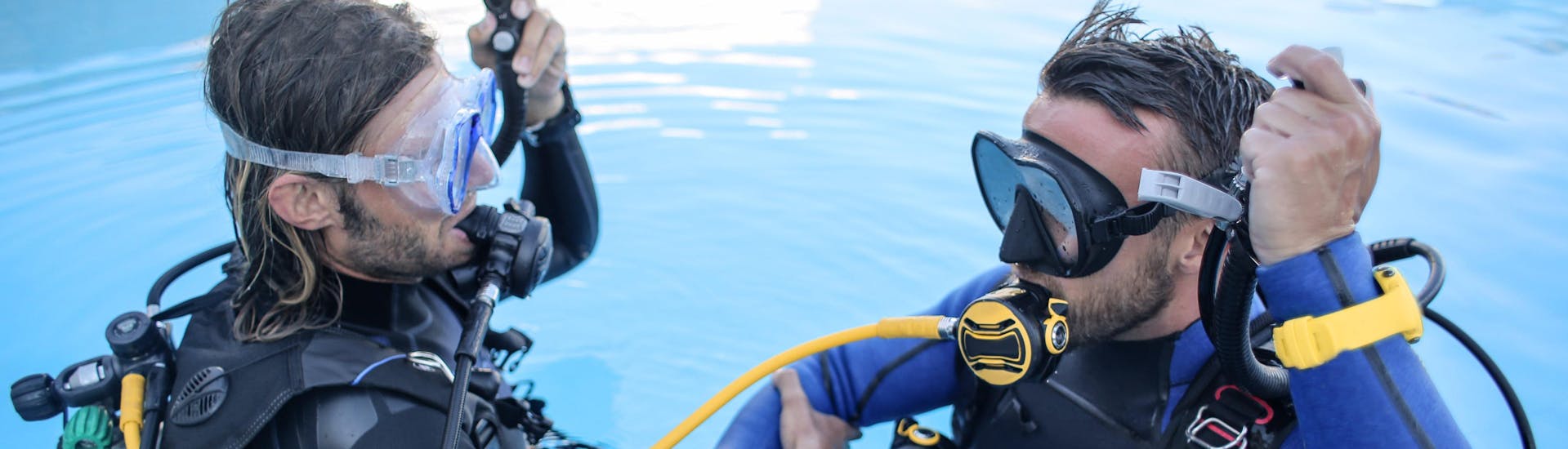 Durante un bautismo de buceo, un instructor de buceo enseña a un alumno a utilizar su equipo de buceo dentro de una piscina.