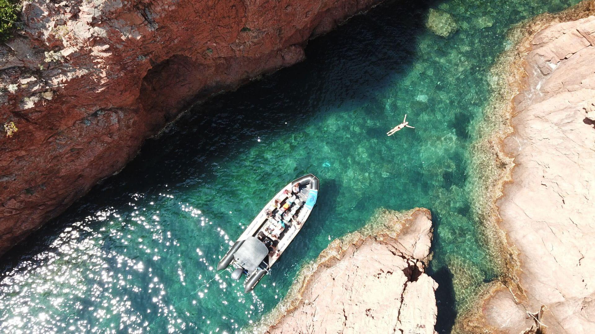 Uno de los barcos Sea You Sun Fréjus & Saint Raphaël en una cala con una persona nadando en las aguas azul turquesa del sur de Francia.