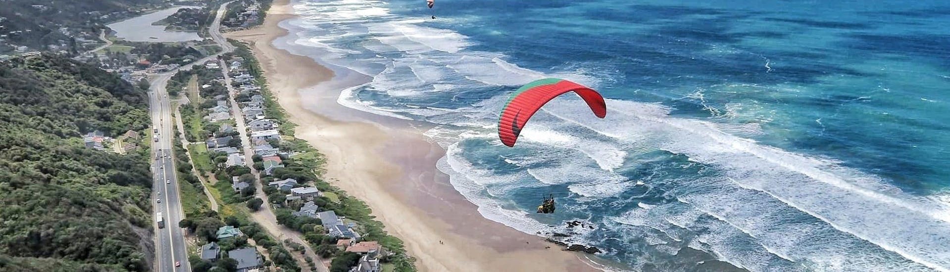 Experienced tandem pilot from Dolphin Paragliding Wilderness is flying with a client above the roaring ocean.