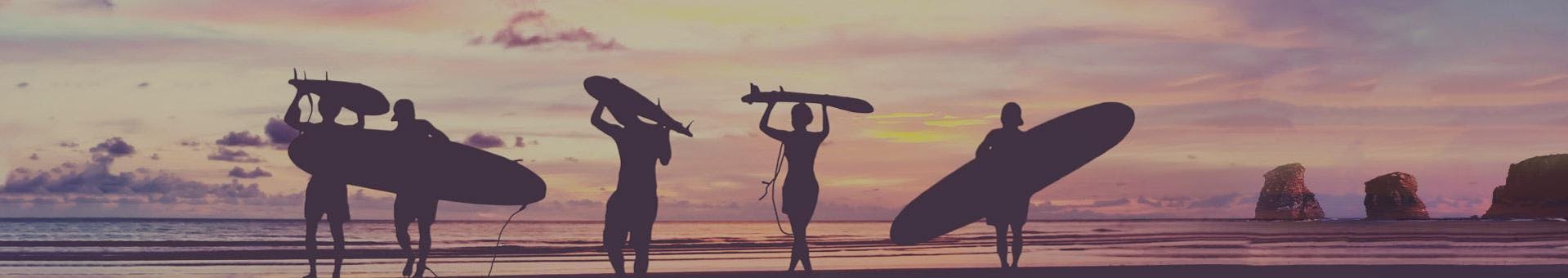 Surfers are walking on the beach at sunset with their surf board on their head or under their arm at the end of their surfing lessons in Hendaye with the surf school École de surf Hendaia.