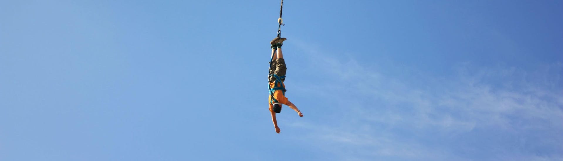 A man is bungee jumping from a bridge in Ardèche under the supervision of a instructor of Elastic Crocodil Bungee. 