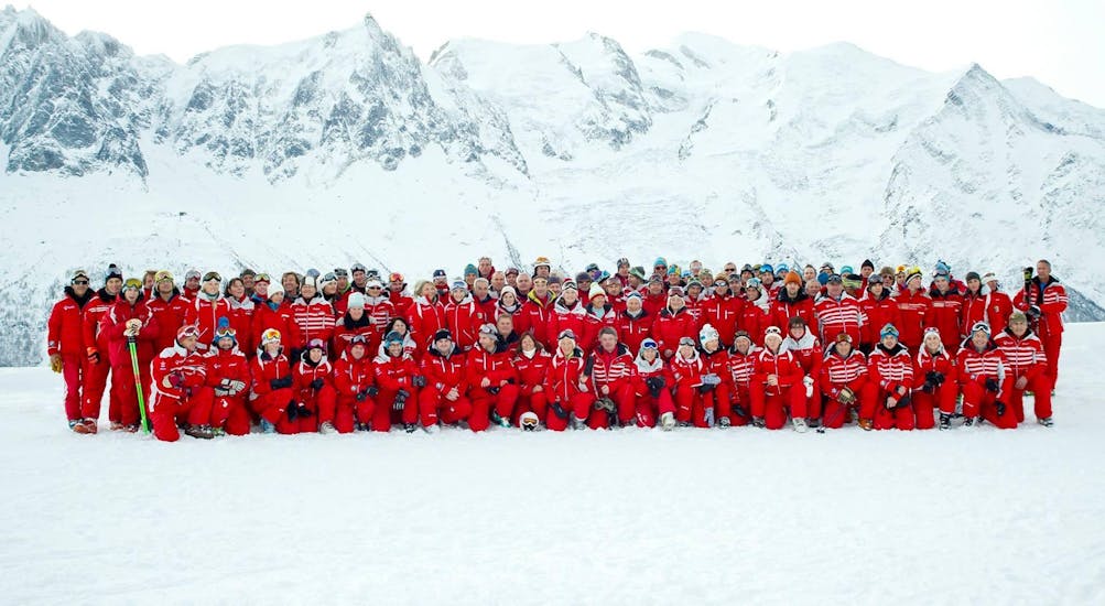 The whole team of the ski school ESF Chamonix is posing for a picture in front of a snow-covered mountain.