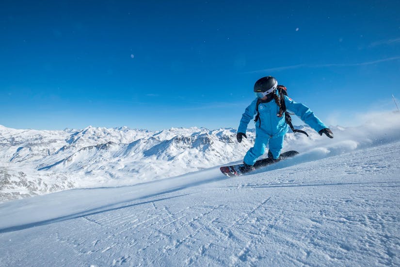 A snowboarding instructor from the ski school ESI Valfréjus is sliding down a snowy slope.