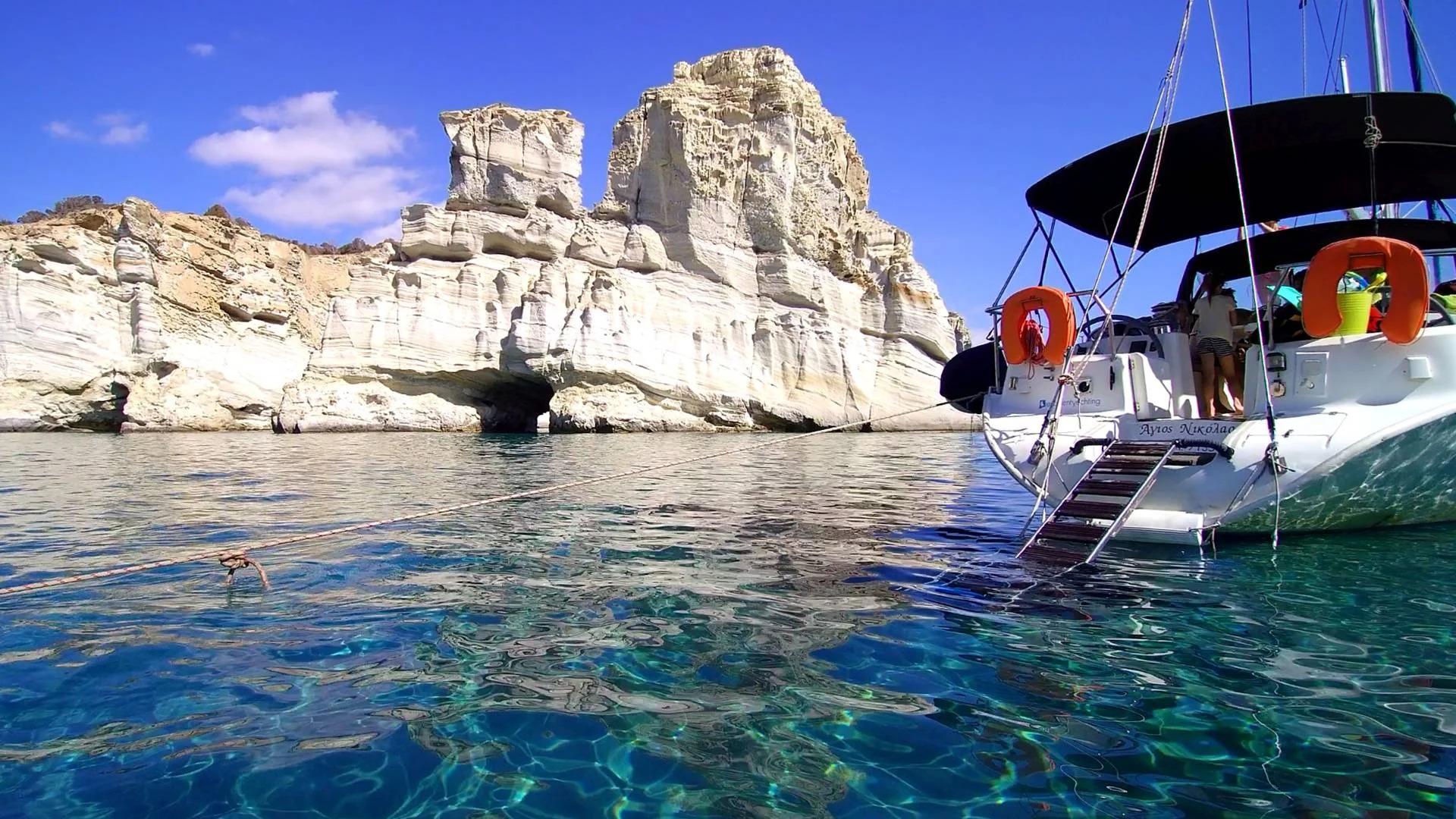 Les falaises blanches près de Milos, l'eau cristalline et turquoise et un bateau d'Excellent Yachting Milos en Grèce.