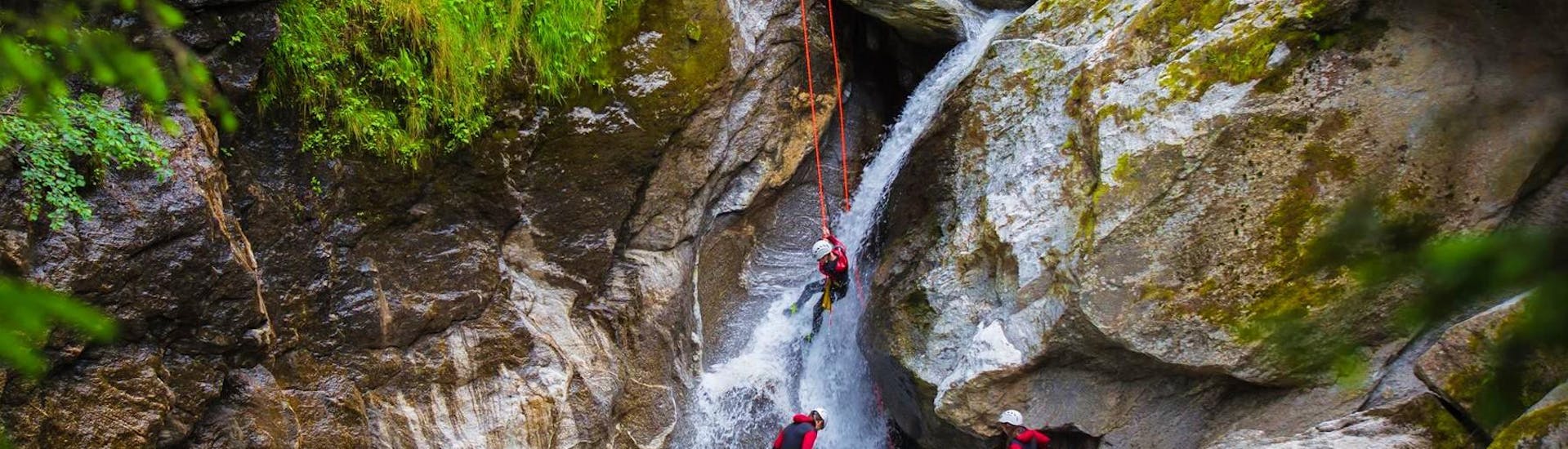 A group of participants is roping down a majestic waterfall during a canyoning tour in the Zillertal valley with Freiluftakademie.