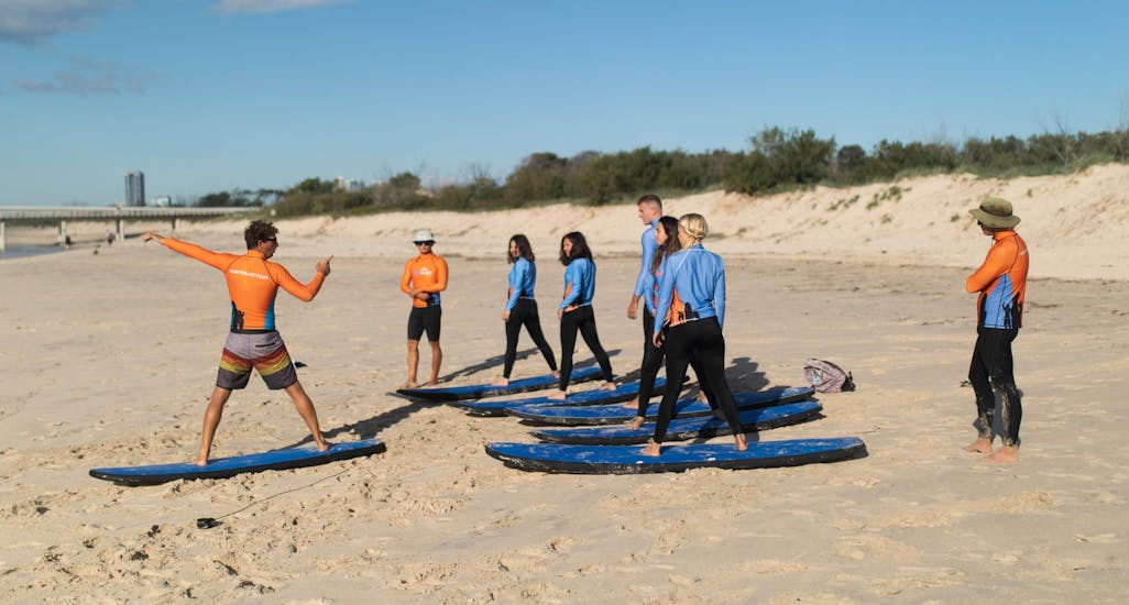 An instructor of Get Wet Surf School is teaching the participants of the surf lessons in Queensland some tricks before entering the water and mastering the surfboard in the water of Gold Coast.