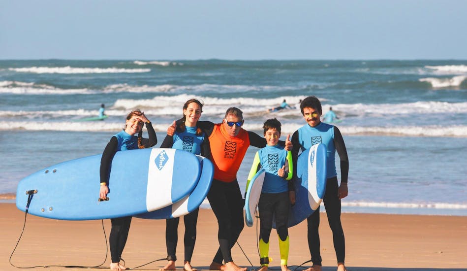 The participants of a surf lesson in Peniche are posing for a picture at the beach with their surf instructor from Go4Surf Peniche.
