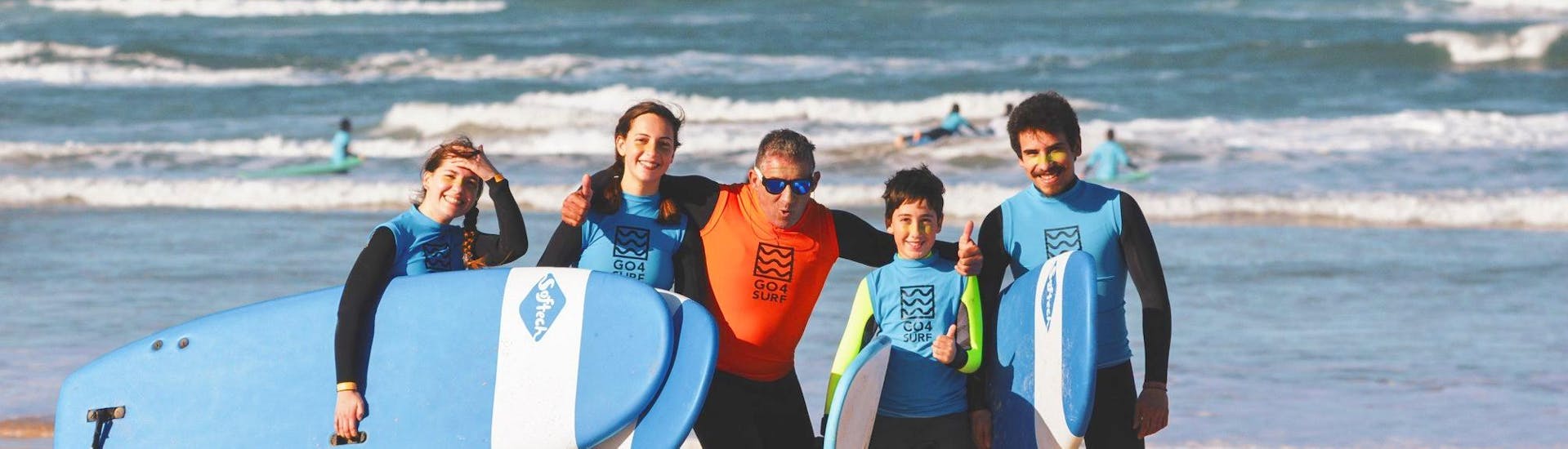 The participants of a surf lesson in Peniche are posing for a picture at the beach with their surf instructor from Go4Surf Peniche.