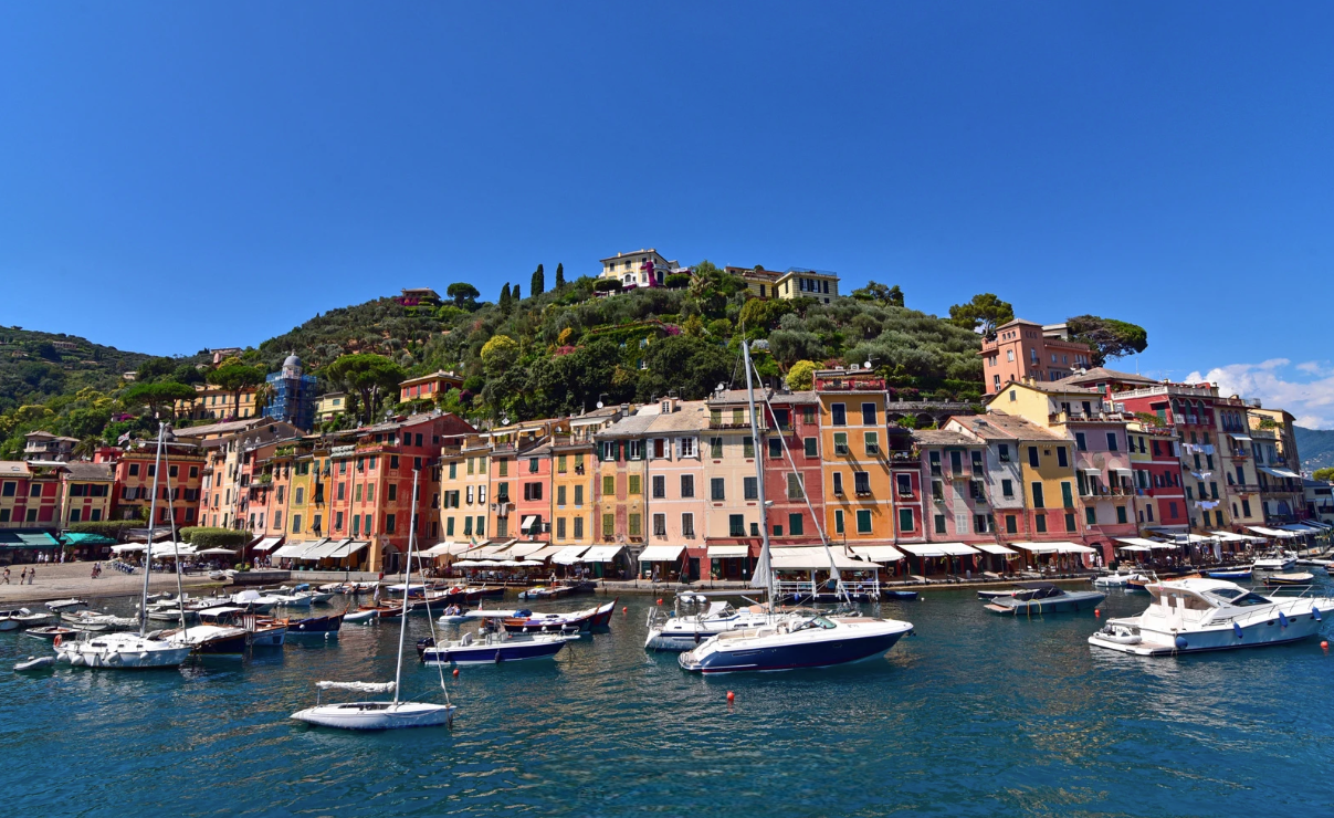 Vista de Portofino desde el mar con edificios coloridos y colinas verdes al fondo.