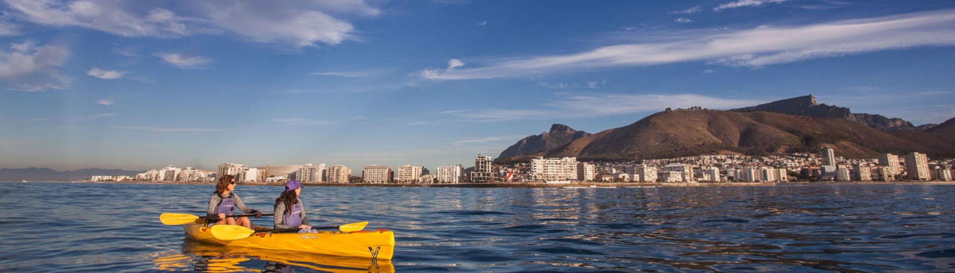 Two women are sea kayaking off the coast of Cape Town, a popular activity offered by Gravity Adventures.